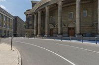 an empty road with columns around it and two people walking by and building behind it