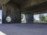 an empty concrete structure near the water under a bridge on a sunny day with some trees in the background