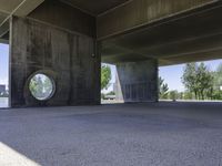 an empty concrete structure near the water under a bridge on a sunny day with some trees in the background