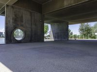 an empty concrete structure near the water under a bridge on a sunny day with some trees in the background