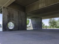 an empty concrete structure near the water under a bridge on a sunny day with some trees in the background