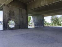 an empty concrete structure near the water under a bridge on a sunny day with some trees in the background