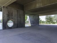 an empty concrete structure near the water under a bridge on a sunny day with some trees in the background