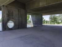 an empty concrete structure near the water under a bridge on a sunny day with some trees in the background