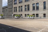 the large building has lots of stone flower containers with flowers inside them on the sidewalk