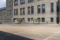 the large building has lots of stone flower containers with flowers inside them on the sidewalk