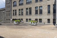 the large building has lots of stone flower containers with flowers inside them on the sidewalk