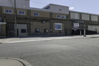 a motorcycle rider and another street sign sit in front of an industrial building on an empty street