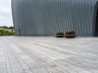 a person sitting on a bench in front of a building that has grey walls and small planters in front