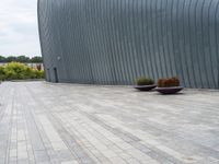 a person sitting on a bench in front of a building that has grey walls and small planters in front