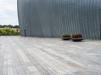 a person sitting on a bench in front of a building that has grey walls and small planters in front