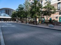 a city street is empty, with benches outside it and an area next to the sidewalk that extends into the building