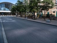 a city street is empty, with benches outside it and an area next to the sidewalk that extends into the building