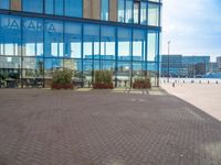 an empty brick path with a glass building in the background with people walking by outside