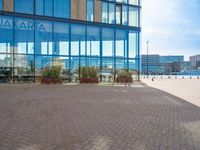 an empty brick path with a glass building in the background with people walking by outside