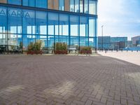 an empty brick path with a glass building in the background with people walking by outside