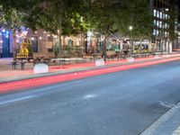 a city street lined with tables and chairs under a string light at night with people walking on the sidewalk