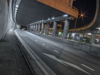 the street is empty under a large bridge at night time under a freeway with white arrows in red and green