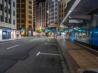 an empty street at night with cars parked and people walking on the sidewalk near buildings