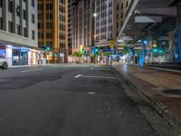 an empty street at night with cars parked and people walking on the sidewalk near buildings