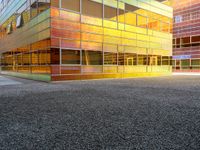 the building has glass windows that look like buildings with orange sky in the background and sidewalk in the foreground