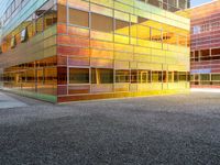 the building has glass windows that look like buildings with orange sky in the background and sidewalk in the foreground