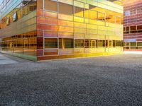 the building has glass windows that look like buildings with orange sky in the background and sidewalk in the foreground