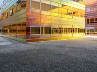 the building has glass windows that look like buildings with orange sky in the background and sidewalk in the foreground