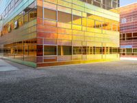 the building has glass windows that look like buildings with orange sky in the background and sidewalk in the foreground