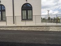 the side of a building has black windows and railings next to an asphalt road