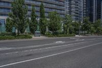 a tall building next to an empty road with trees in front of it, and a row of parked cars beside