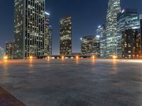 several high rise buildings in a big city at night time on an empty street, with a concrete floor in front