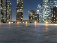 several high rise buildings in a big city at night time on an empty street, with a concrete floor in front