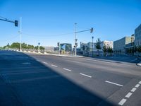 a street in the middle of an empty area with two stop lights and the right side is blue sky