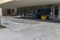 the outside entrance of an empty business with trash containers on both sides of it and a parking sign sitting on the side of the sidewalk