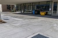 the outside entrance of an empty business with trash containers on both sides of it and a parking sign sitting on the side of the sidewalk