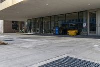 the outside entrance of an empty business with trash containers on both sides of it and a parking sign sitting on the side of the sidewalk