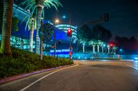 an empty city road with palm trees and a building illuminated at night in the background