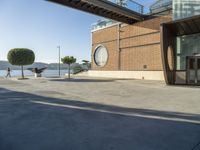 a skateboarder is going down the street beside the water and some buildings and people are out on a sunny day