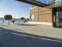 a skateboarder is going down the street beside the water and some buildings and people are out on a sunny day