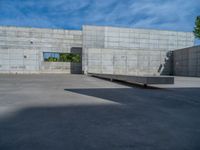 the empty parking lot in front of a wall with apartment buildings on it and a skateboarder on a ramp