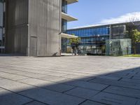 some green grass and an empty courtyard with buildings in the background and a person on a phone