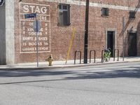 a green bicycle sits parked by the side of a building on a road with bicycles parked in front