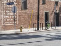 a green bicycle sits parked by the side of a building on a road with bicycles parked in front