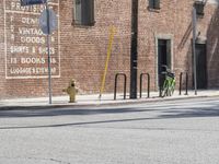 a green bicycle sits parked by the side of a building on a road with bicycles parked in front