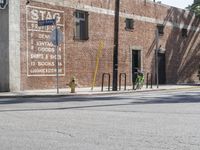 a green bicycle sits parked by the side of a building on a road with bicycles parked in front