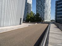 a paved city road with modern office buildings in the background on a sunny day and a railing on either side