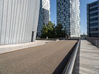 a paved city road with modern office buildings in the background on a sunny day and a railing on either side