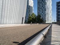 a paved city road with modern office buildings in the background on a sunny day and a railing on either side