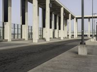 an empty sidewalk that has some columns in it under a blue sky with clouds on the top